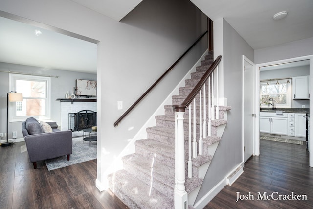 stairway with a healthy amount of sunlight, a brick fireplace, baseboards, and wood finished floors