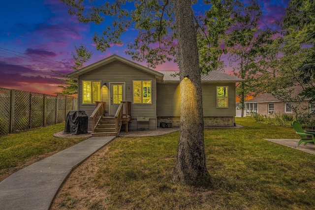 view of front of property with metal roof, a lawn, and fence