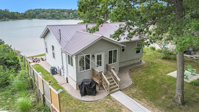 exterior space featuring a water view, a lawn, central AC, a fenced backyard, and metal roof