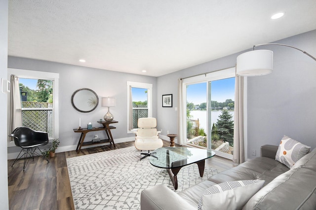 living room featuring wood finished floors, baseboards, recessed lighting, a water view, and a textured ceiling