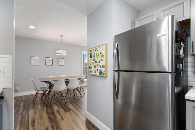 kitchen featuring baseboards, light countertops, freestanding refrigerator, wood finished floors, and hanging light fixtures