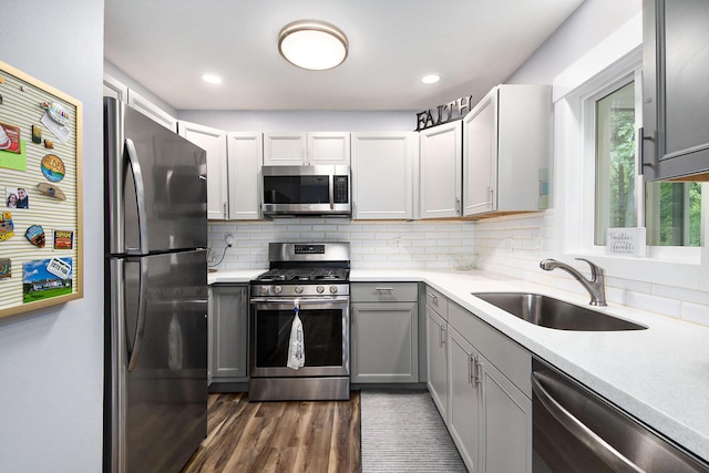 kitchen with light countertops, decorative backsplash, gray cabinets, stainless steel appliances, and a sink