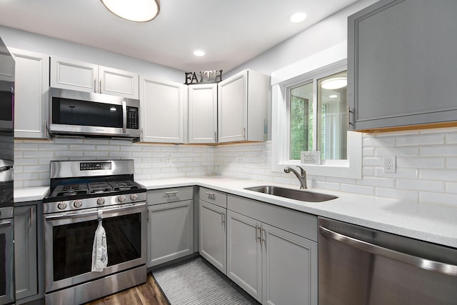 kitchen featuring gray cabinetry, a sink, tasteful backsplash, stainless steel appliances, and light countertops