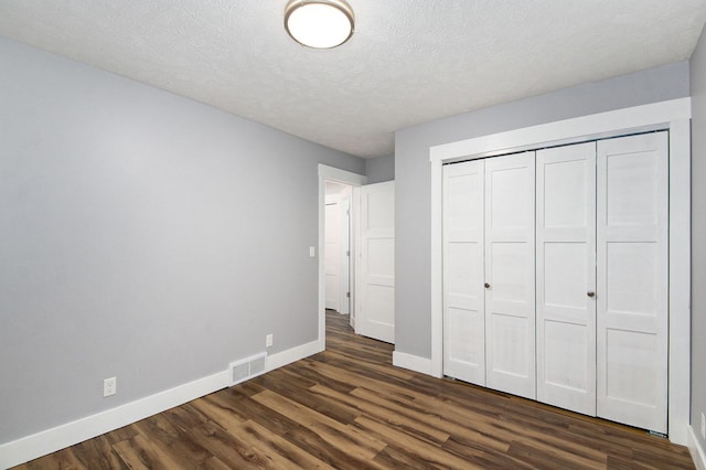 unfurnished bedroom featuring visible vents, dark wood-type flooring, baseboards, a closet, and a textured ceiling