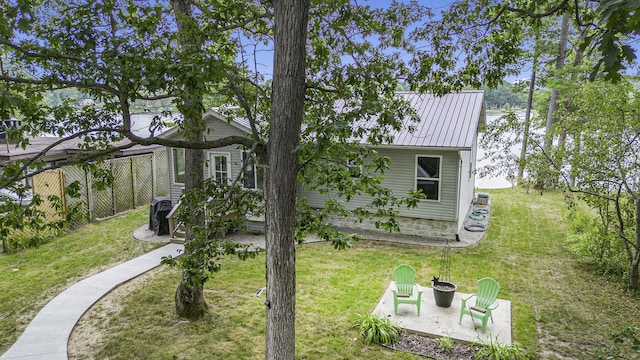 rear view of house with fence, a standing seam roof, a yard, a patio area, and metal roof