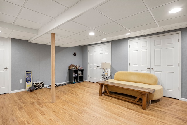 living area featuring a drop ceiling, baseboards, and light wood-style flooring