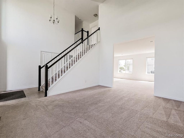 unfurnished living room featuring a notable chandelier, stairway, a high ceiling, and carpet floors