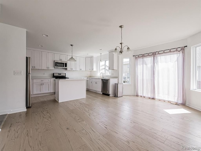 kitchen with a kitchen island, stainless steel appliances, light countertops, decorative light fixtures, and light wood-type flooring