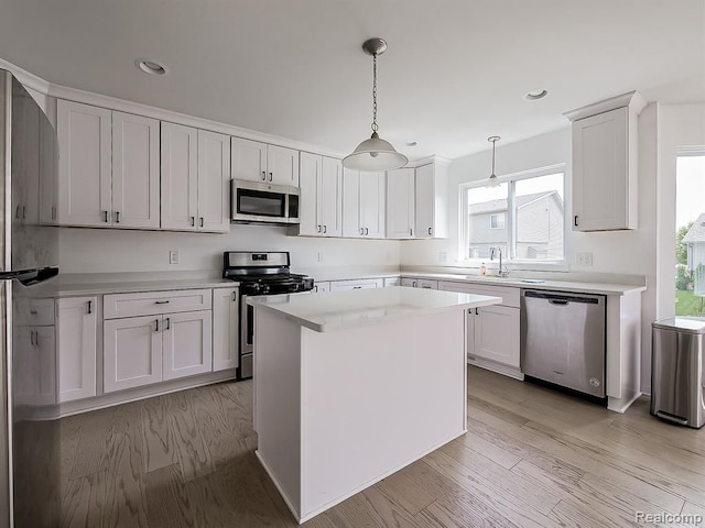 kitchen featuring light wood finished floors, pendant lighting, light countertops, appliances with stainless steel finishes, and a sink