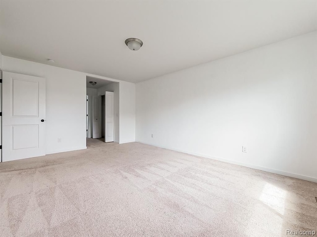 empty room featuring baseboards and light carpet