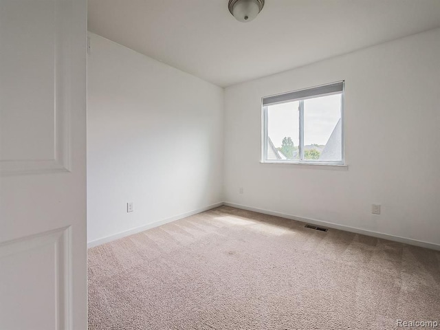 empty room featuring baseboards, visible vents, and light carpet