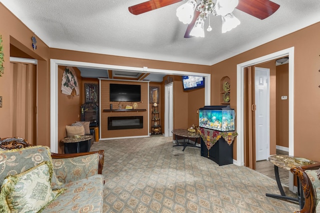 carpeted living area featuring baseboards, a textured ceiling, a glass covered fireplace, and a ceiling fan