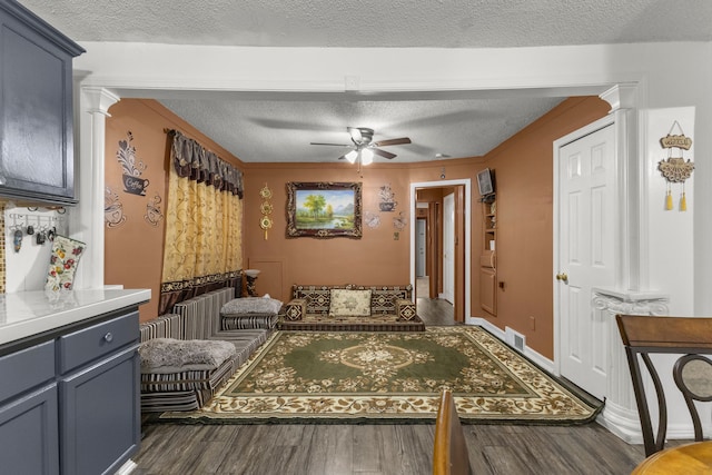 living area with a ceiling fan, decorative columns, wood finished floors, and visible vents