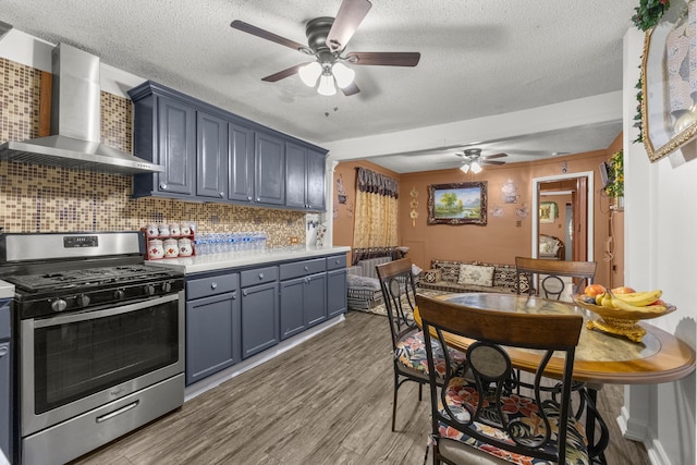 kitchen featuring light wood-type flooring, wall chimney range hood, gas stove, light countertops, and decorative backsplash