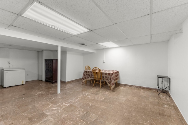 finished basement featuring a drop ceiling, white refrigerator, and baseboards