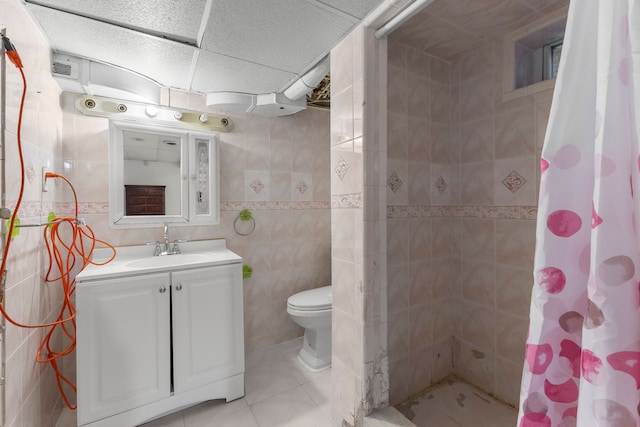 full bath with vanity, a tile shower, tile patterned flooring, tile walls, and toilet