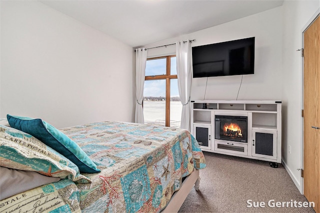 bedroom featuring baseboards, a glass covered fireplace, and carpet flooring