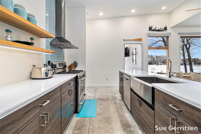 kitchen featuring stainless steel range with gas cooktop, open shelves, a sink, dark brown cabinets, and wall chimney range hood