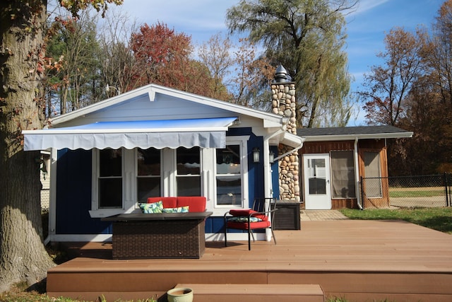 rear view of house featuring a wooden deck, a chimney, and fence