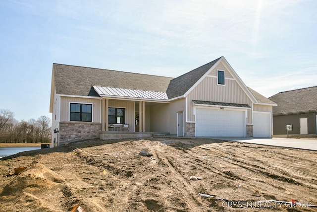 view of front of property featuring a standing seam roof, stone siding, concrete driveway, an attached garage, and metal roof