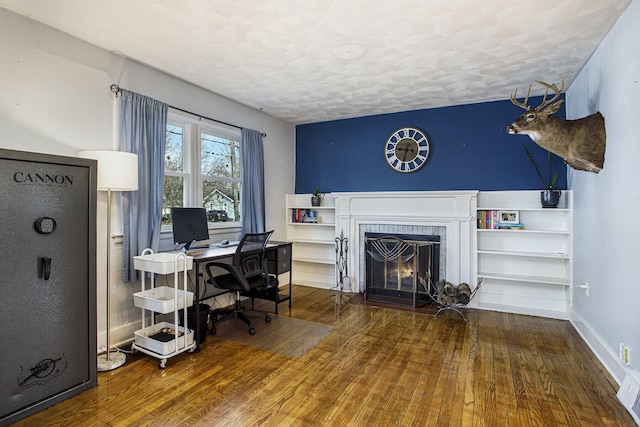 office area featuring wood finished floors, a fireplace, baseboards, and a textured ceiling