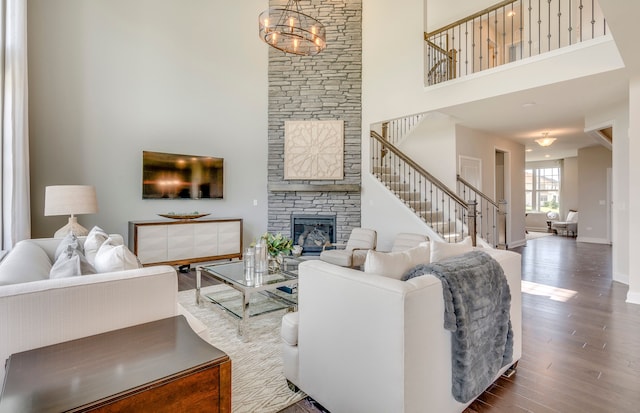 living room featuring baseboards, stairway, a stone fireplace, a high ceiling, and wood finished floors