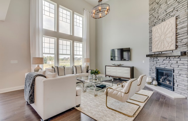 living area with wood finished floors, baseboards, a high ceiling, a stone fireplace, and a chandelier