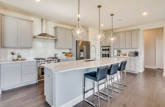 kitchen with backsplash, high quality appliances, dark wood-style floors, wall chimney exhaust hood, and a sink