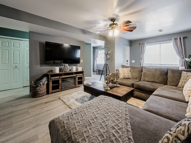 living room featuring a glass covered fireplace, visible vents, wood finished floors, and a ceiling fan