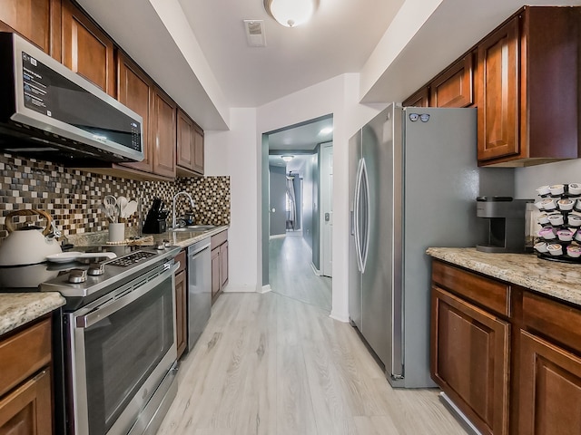 kitchen with tasteful backsplash, light wood finished floors, light stone countertops, stainless steel appliances, and a sink