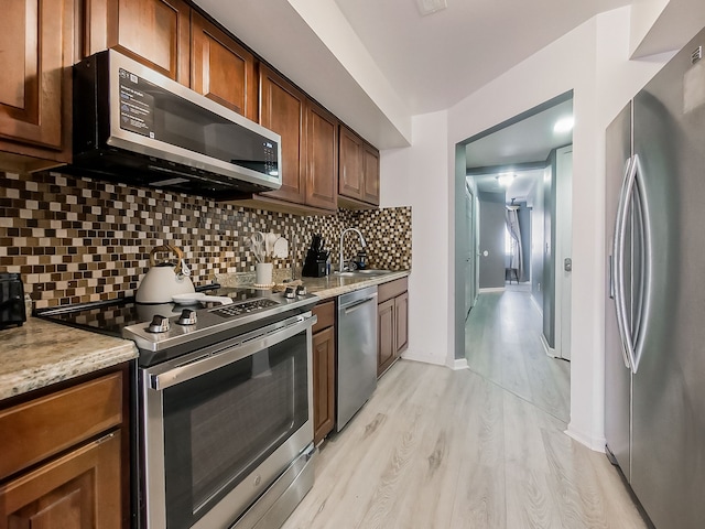 kitchen with a sink, stainless steel appliances, light wood finished floors, decorative backsplash, and baseboards