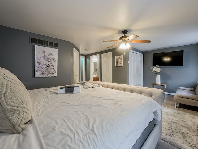 bedroom featuring visible vents, multiple closets, a ceiling fan, wood finished floors, and baseboards