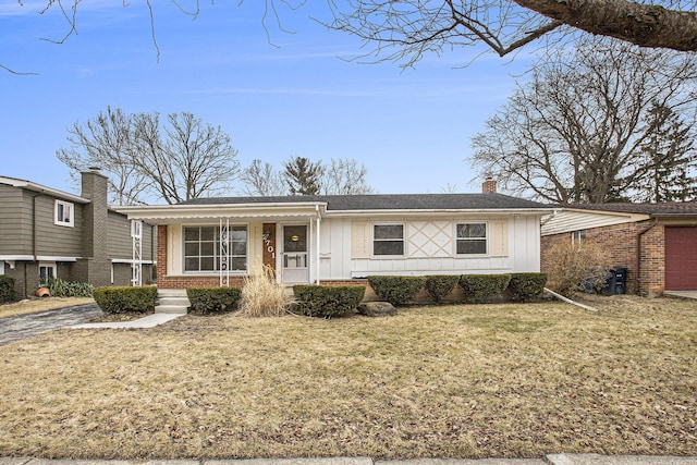 view of front facade with a front yard, covered porch, a chimney, board and batten siding, and brick siding