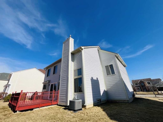 rear view of property featuring a deck, a lawn, a chimney, and central AC