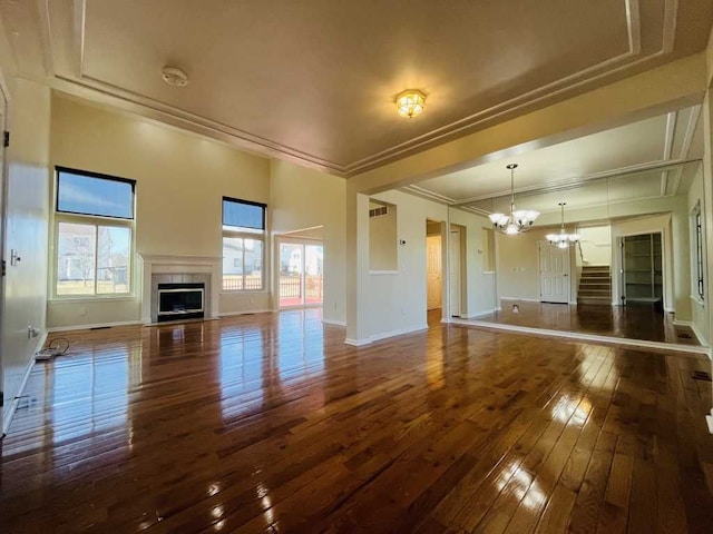 unfurnished living room featuring baseboards, an inviting chandelier, a fireplace with flush hearth, hardwood / wood-style flooring, and crown molding