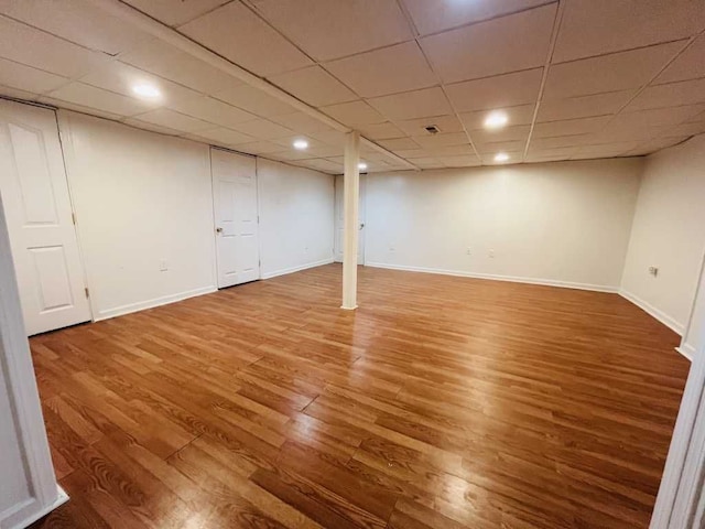 finished below grade area with a drop ceiling, baseboards, and wood finished floors