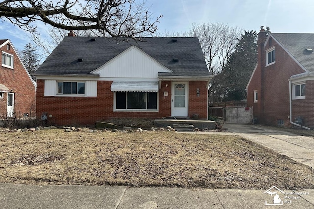 bungalow featuring brick siding, a shingled roof, and a gate