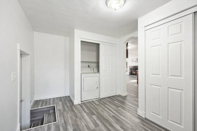 clothes washing area featuring wood finished floors, laundry area, arched walkways, a glass covered fireplace, and washing machine and dryer