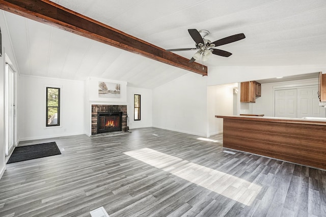 unfurnished living room with baseboards, ceiling fan, lofted ceiling with beams, a fireplace, and wood finished floors