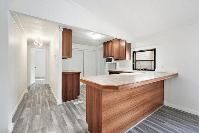 kitchen with white microwave, baseboards, tile countertops, brown cabinets, and wood finished floors