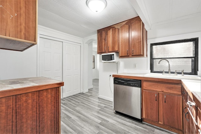 kitchen featuring a sink, arched walkways, light wood finished floors, white microwave, and dishwasher