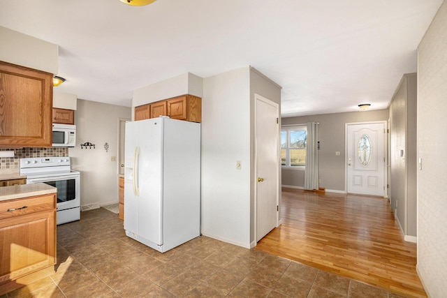 kitchen with white appliances, brown cabinetry, baseboards, light countertops, and backsplash