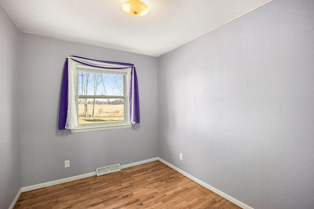 empty room with wood finished floors, visible vents, and baseboards