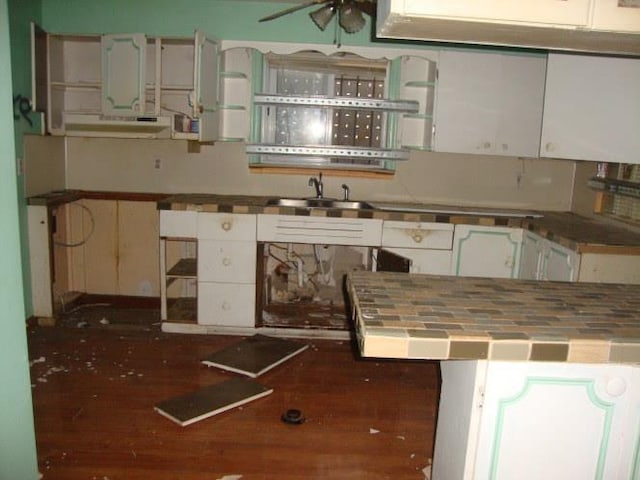 kitchen with a sink, under cabinet range hood, tile countertops, white cabinets, and open shelves