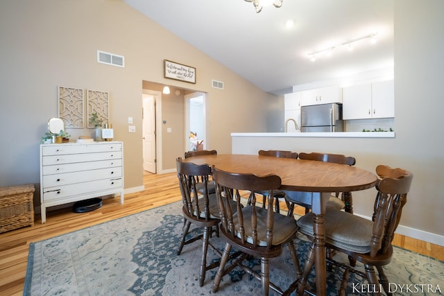 dining room with visible vents, light wood finished floors, baseboards, and vaulted ceiling