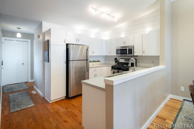 kitchen with light wood finished floors, stainless steel appliances, a peninsula, light countertops, and vaulted ceiling