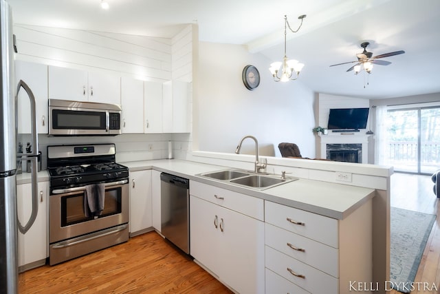 kitchen with a sink, light wood-style floors, appliances with stainless steel finishes, and a peninsula