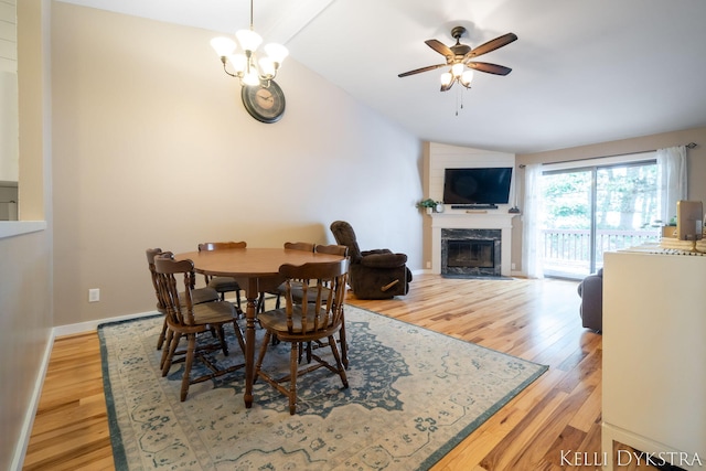 dining area with light wood-type flooring, baseboards, a premium fireplace, and vaulted ceiling