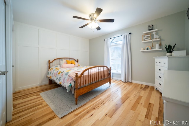 bedroom featuring a ceiling fan, a decorative wall, and light wood-style floors