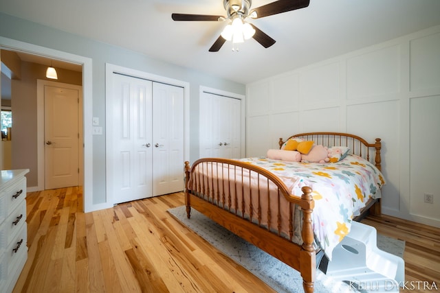 bedroom with light wood finished floors, two closets, ceiling fan, and a decorative wall